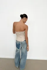 Top tipo corset de escote corazón y hombros descubiertos, con varillas interiores para estructura. Presenta cierre frontal con ganchos metálicos y ajuste en la espalda mediante cordones cruzados.