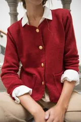 Cardigan de punto color beige con cuello redondo, cierre frontal con botones dorados, bolsillos frontales y terminaciones en crochet. Presenta hombreras internas y diseño de corte recto.