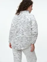Buzo de dormir de tela fleece con estampado animal print en tonos grises y blancos. Presenta cuello alto con cierre de botones a presión y mangas largas.