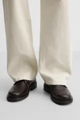 Zapato tipo blucher fabricado en piel de alta calidad, con cordonera de cinco pasados, horma redonda y suela a tono con ligero tacón.