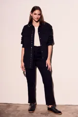 Sobrecamisa negra de algodón con corte oversize, cuello clásico, cierre frontal con botones a presión, dos bolsillos de parche en el pecho y apliques metálicos en cuello y solapa.