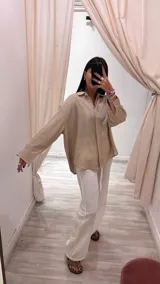 Camisa oversize color beige con brillo sutil, cuello camisero, manga larga con puños y cierre frontal abotonado.