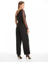 Enterito largo de crepe color negro con diseño asimétrico de un solo hombro. Presenta una manga larga de tela mesh transparente y pierna de corte recto y fluido con bolsillos laterales invisibles.