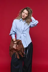Camisa blanca de manga larga con volumen y estructura, cierre frontal con botones y lazo ajustable en la cintura que realza la silueta.