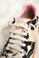 Zapatillas bajas de cuero con estampado de vaca en blanco y negro, cordones marrones y suela de goma color caramelo.