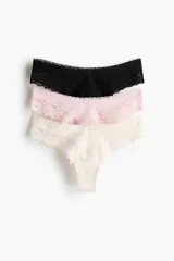 Pack de tres bombachas tipo brazilian de tiro bajo con cintura en V, confeccionadas en punto de algodón y encaje. Incluye una bombacha negra, una rosada y una beige.