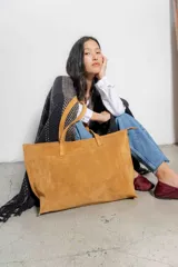 Bolso tipo tote de gamuza color tostado, con doble asa de hombro y cierre superior con cremallera.