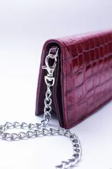 Cartera negra con textura símil cocodrilo y cadena metálica plateada.