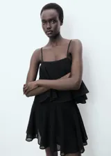 Vestido corto negro de punto fino, sin mangas, con tirantes finos, escote cuadrado y maxi volante superpuesto en el pecho con diseño evasé.