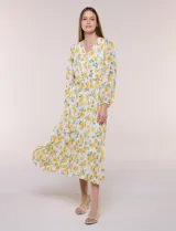 Vestido maxi de gasa con estampado floral en tonos amarillos y verdes sobre base blanca, escote en V cruzado, mangas largas y cintura elastizada con lazo.