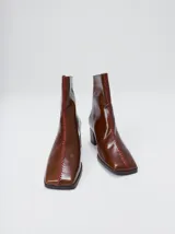 Botas de caña media color marrón, confeccionadas en cuero con acabado brillante. Presentan punta cuadrada, taco de madera y un distintivo bordado decorativo en color rojo que recorre el empeine hasta la punta.