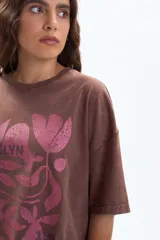 Remera oversize de manga corta color marrón con efecto desgastado y estampado frontal en rosa de hojas y la palabra "BROOKLYN".