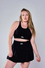 Conjunto deportivo compuesto por un top tipo bra de escote redondo y una pollera tableada corta, ambos en color negro con el logo 'bk.' estampado en blanco en la banda elástica.