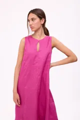 Vestido largo color beige, sin mangas, con escote redondo y abertura en forma de gota en el pecho. Tiene corte holgado y ruedo con volantes.