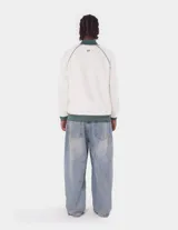 Campera deportiva de tejido doble faz color blanco roto, con cuello, puños y cintura en verde oscuro. Presenta mangas raglán con doble franja verde oscuro y blanco, cierre frontal y logo bordado en el pecho.