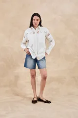 Sobrecamisa blanca de algodón con bordados florales calados en mangas, cuello y pechera. Corte oversize, manga larga y dos bolsillos frontales.