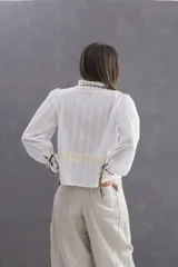 Camisa de voile de algodón en color blanco, con diseño romántico y corte holgado. Presenta detalles de encaje en color marfil en el frente y la espalda, cuello con blonda y pasa cinta, y mangas largas ligeramente fruncidas en los hombros con puños decorados.