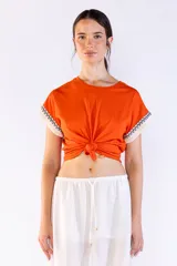 Remera de manga corta color naranja, confeccionada en algodón, con detalles de flecos y bordado en las mangas.