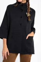 Cardigan negro de corte oversize, con cuello alto, cierre frontal de botones y mangas tres cuartos. Presenta un diseño holgado con bolsillos frontales y una caída fluida.
