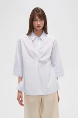 Blusa de algodón a rayas verticales celestes y blancas, holgada, con cuello camisero y mangas 3/4.