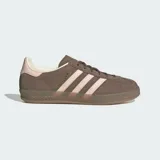 Championes Adidas Gazelle Indoor de diseño clásico, confeccionados en gamuza color marrón con las icónicas tres tiras laterales y refuerzo en el talón en color rosado. Presentan suela de goma translúcida y cierre de cordones.