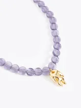 Collar de cuentas de vidrio color ámbar con un charm dorado en forma de llama en el centro. Incluye cadena de extensión y cierre de mosquetón.