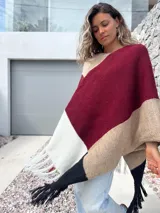 Poncho tejido de punto con diseño de bloques de color en tonos bordó, beige, blanco y negro, con terminación de flecos en el ruedo.