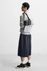 Bandolera color verde militar con acabado engomado, correa de hombro ajustable y extraíble, compartimento principal con cierre de cremallera, bolsillo interior con cremallera y bolsillo frontal con cierre de hebilla de liberación rápida.