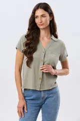 Camisa lisa de lino color beige, de manga corta, con cuello camisero, bolsillo ojal en el pecho y cierre frontal con botones.