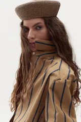 Camisa boxy de popelina de algodón color tostado con diseño de rayas verticales oscuras, cuello camisero, botones frontales y mangas largas con puños estampados a cuadros.