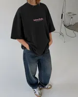 Remera oversize negra con diseño gráfico en la espalda que incluye la inscripción "Kaboa Radio" y un personaje ilustrado, de corte amplio y mangas cortas.