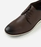 Zapato de vestir acordonado color marrón oscuro, de cuero, con suela blanca y detalles de costuras.