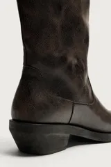 Bota estilo cowboy de caña media, confeccionada en cuero con acabado desgastado. Presenta horma cuadrada, tiradores laterales y suela con tacón bloque.