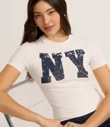 Remera de algodón color crudo, corte new t-shirt ajustado al cuerpo, con cuello redondo y manga corta. Estampa frontal con las letras 'NY' en azul con efecto desgastado.