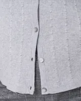 Cardigan blanco de tejido liviano con trama en relieve, cuello a la base y cierre frontal con botones a tono. Presenta mangas tres cuartos.