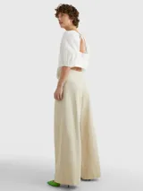 Pantalón beige de pierna ancha confeccionado en sarga de mezcla de algodón orgánico, lyocell y lino. Presenta pinzas en la parte delantera, cierre de cremallera con botón y logo de Tommy Hilfiger bordado en la parte trasera.