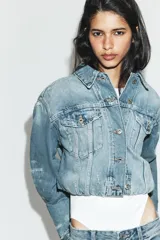 Cazadora de denim crop con cuello solapa, manga larga y cierre frontal con botones. Presenta efecto lavado, bolsillos de plastrón con solapa en el pecho y detalles de rotos.