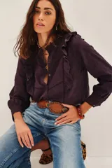 Camisa blanca de algodón con diseño romántico, cuello alto con volados, cierre frontal de botones y detalles de encaje y bordados calados. Presenta mangas largas con puños de encaje y volados frontales.