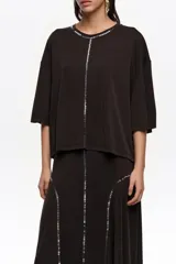 Remera corta de corte boxy y color negro, con escote redondo, mangas cortas y aplicación de lentejuelas en el contorno del cuello y formando una línea vertical central.