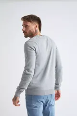 Sweater de tejido de punto color beige, con escote en V, mangas largas y puños y dobladillo acanalados. Presenta un pequeño logo bordado en el pecho.