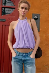 Top corto de cuello halter con diseño delantero cruzado y bajo abullonado con elástico. Presenta un estampado sutil de lunares y cierre en la espalda con botones ocultos.