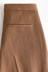 Pantalón sastrero de corte holgado color marrón, con pretina prolongada, cierre frontal y pinzas en las perneras amplias.