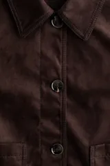 Chaqueta corta marrón de acabado cepillado suave tipo gamuza, con cuello clásico, cierre frontal de botones, dos bolsillos de parche delanteros y mangas largas.