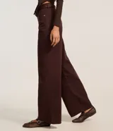 Pantalón wide leg de sarga color marrón oscuro, de talle alto con trabillas para cinturón, cierre de botón y cremallera, con bolsillos delanteros y traseros.