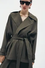 Chaqueta fluida de Zara, con cuello solapa, manga larga ajustable con trabilla y botón, y cinturón del mismo tejido con lazada. Presenta un diseño de corte recto y forro interior a tono.