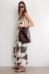Vestido midi de corte holgado con cuello halter ajustable mediante lazada y hombros descubiertos. Presenta un diseño con tiras cruzadas en la espalda y un estampado abstracto en tonos rosado, verde y marrón sobre fondo blanco.