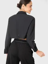 Blusa corta negra de manga larga con cuello camisero y dos bolsillos frontales con fuelle. Se puede usar abierta o cerrada. Combina con el pantalón Domi.