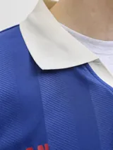 Camiseta de estilo polo con cuello camisero, manga corta y calce relajado. Presenta un diseño en color azul con estampado frontal "FIFA WORLD CUP" y detalles gráficos en contraste. Confeccionada en tejido técnico de poliéster reciclado.