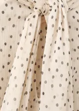 Blusa de gasa color beige con estampado de lunares negros, cuello alto con lazo integrado y mangas largas con puños amplios.