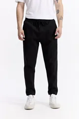 Pantalón de jogging negro de algodón y poliéster, con puños ajustados en los tobillos, cintura elástica con cordón y costuras verticales marcadas en el frente.